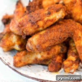 A plate filled with crispy, golden brown dry rub air fryer wings stacked on top of each other. The wings are seasoned with visible spices and appear to be freshly cooked. The edges of the plate are slightly visible, making this recipe a feast for both the eyes and taste buds.