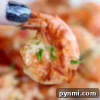 Close-up of a hand with glittery black nails holding a perfectly cooked shrimp, garnished with herbs, straight from the air fryer.