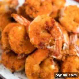 A plate of golden-brown, crispy air fryer fried shrimp stacked in a pile, showcasing a crunchy texture with visible seasonings.