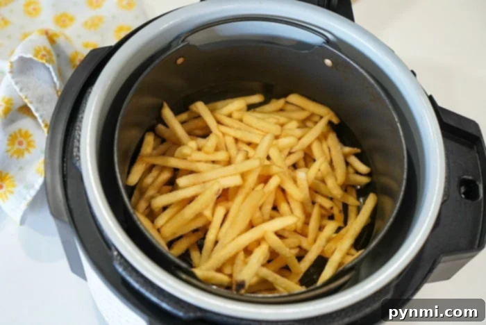 Crispy Air Fryer Fish and Chips 6 Crispy French fries sit beside a yellow floral cloth, freshly golden from the air fryer. Perfectly paired with delicious ninja foodi fish and chips for a delightful meal.