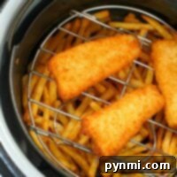 Golden fish fillets and crispy fries sizzle perfectly on a rack, transforming into a delightful serving of air fryer fish and chips.