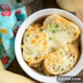 A bowl of pressure cooker French onion soup, topped with melted cheese and bread slices, sits tantalizingly next to a fresh onion and rustic bread loaf.