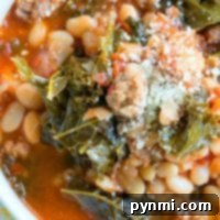 A bowl of pressure cooker sausage soup with white beans, kale, tomato broth, and grated cheese on top.