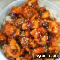 A bowl of air fryer teriyaki chicken bites glazed to perfection, garnished with sesame seeds and chives, served over white rice.