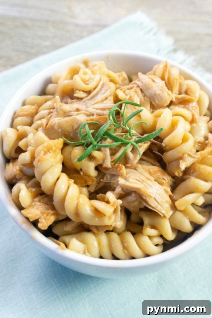 A bowl of rotini pasta with shredded turkey, subtly scented with fresh rosemary, sits gracefully on a light blue napkin beside an instant pot turkey tenderloin. - A hearty bowl of rotini pasta and shredded turkey, garnished with fresh rosemary, served alongside the cooked tenderloin.