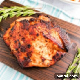 air fryer boneless turkey breast with a crispy exterior rests on a wooden board, adorned with sprigs of rosemary. In the background, an air fryer turkey breast and a bowl of roasted potatoes sit charmingly on a striped cloth.
