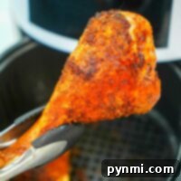 Using tongs, a crispy, seasoned turkey leg is held above the air fryer, showcasing its golden perfection.