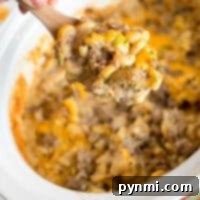 A hand holds a wooden spoon above a crockpot filled with a cheesy hamburger casserole. This savory delight combines macaroni, ground beef, and melted cheese, all garnished with fresh herbs for that perfect finish.