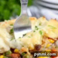 Close-up of a fork in a plate of Shepherd's Pie with ground beef, surrounded by vibrant vegetables and creamy mashed potatoes.