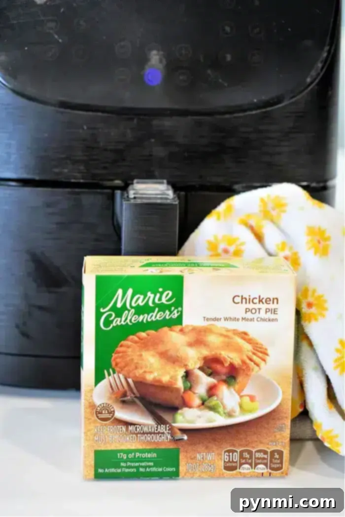 Crispy Air Fryer Frozen Pot Pie 2 A Marie Callender's frozen pot pie box is placed in front of a black air fryer, ready for a crispy finish. A dish towel with yellow flowers is draped beside it, adding a touch of warmth to the scene.