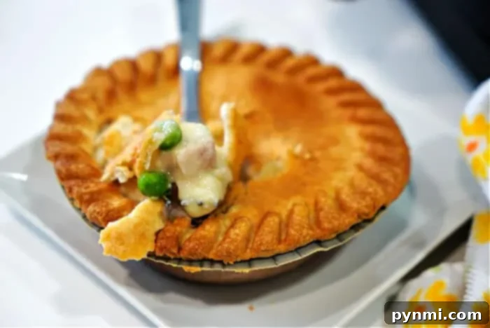 Crispy Air Fryer Frozen Pot Pie 10 A fork lifts a bite of creamy chicken pot pie with peas and carrots, fresh from a frozen pot pie cooked to perfection in an air fryer. The flaky, golden-brown crust has a beautiful fluted edge, and a patterned cloth is partially visible beside the white plate.