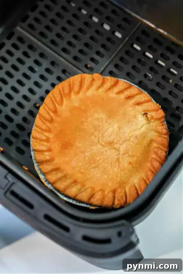 Crispy Air Fryer Frozen Pot Pie 6 A golden-brown frozen pot pie sits in an air fryer basket, its crust evenly baked with a decorative crimped edge. The air fryer features a perforated base for optimal air circulation, making it perfect for transforming frozen delights into crispy perfection.