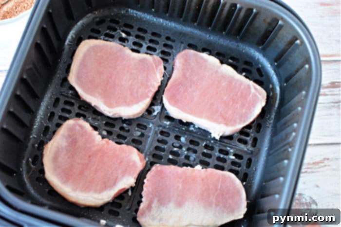 Air fryer basket filled with beautifully seasoned frozen pork chops beginning to cook, showing a crispy golden crust forming.