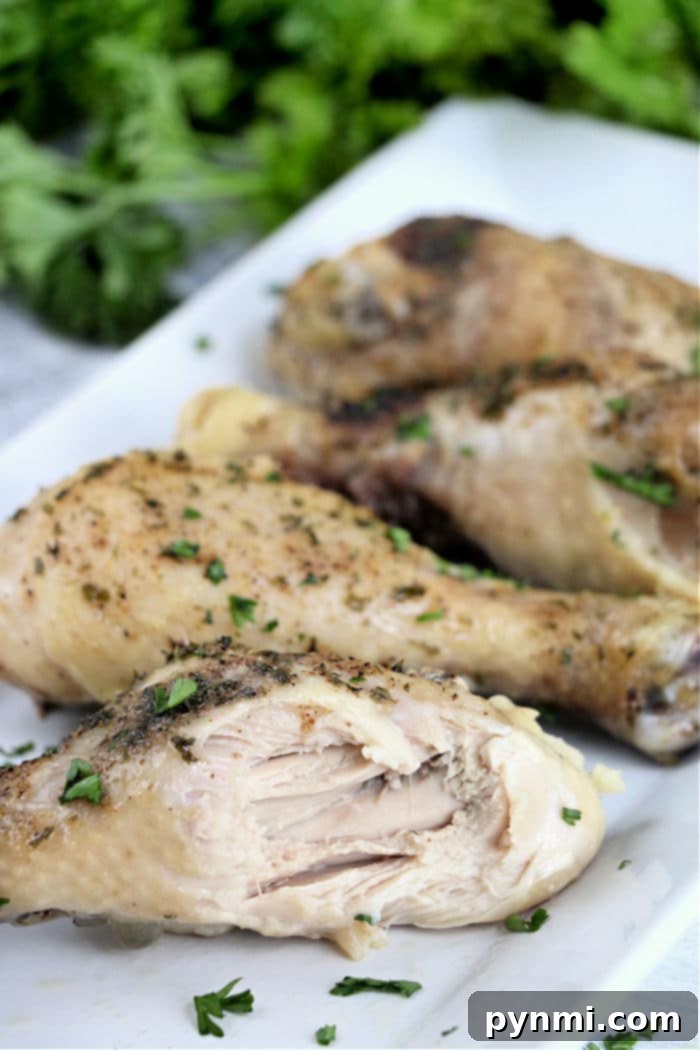 Fall-Off-The-Bone Slow Cooker Chicken Legs 7 Slow-cooked chicken legs rest on a white plate, garnished with fresh herbs.