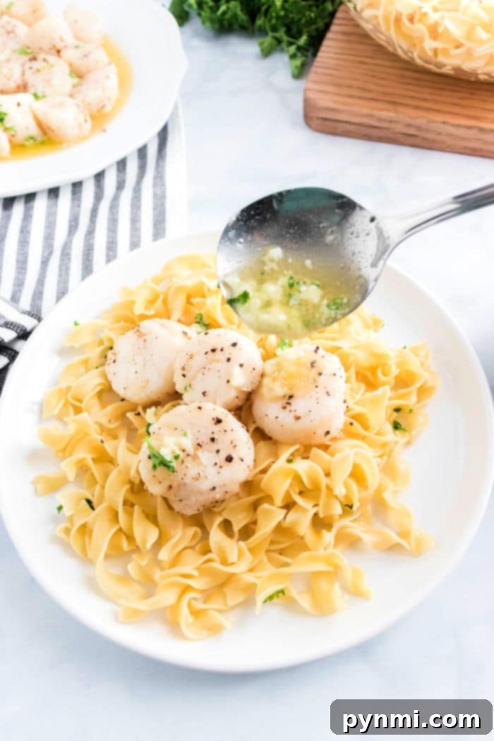 Golden Air Fryer Scallops 2 Plate of pasta topped with perfectly seared air fryer scallops and savory sauce, served with a spoon and striped napkin.