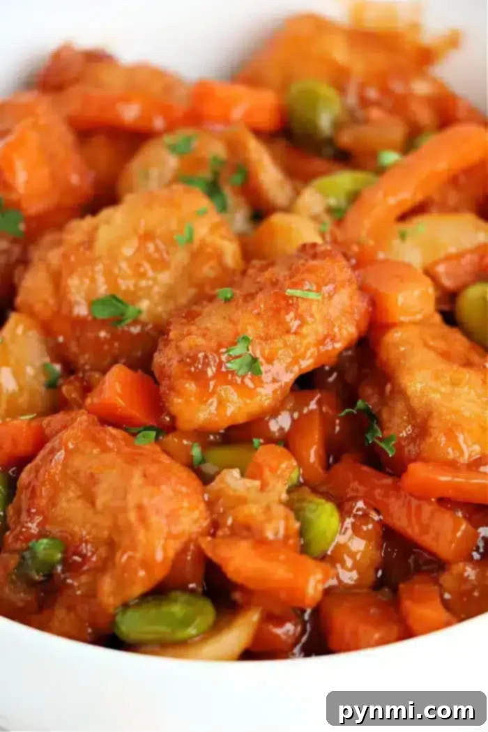Trader Joe's Orange Chicken Air Fryer Secret to Crispy Perfection 6 A close-up of sweet and sour air fryer chicken with crispy breaded pieces, sliced carrots, edamame, and a glossy sauce. Garnished with chopped parsley.