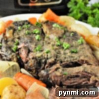 Tender pot roast with carrots, potatoes, and onions on a white plate in front of a slow cooker—perfect for making even a frozen roast in the slow cooker.