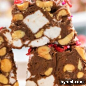 A close-up of no-bake chocolate marshmallow squares showcases rocky road fudge adorned with marshmallows, peanuts, and vibrant red sprinkle toppings on a plate.