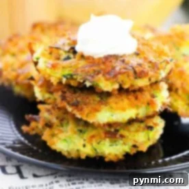A stack of air fryer zucchini fritters topped with sour cream sits elegantly on a black plate.