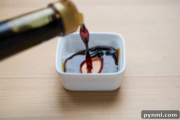 Soy Sauce: Unpacking the Umami Essential 4 A small stream of coconut aminos are like soy sauce, an ancient and savory condiment, cascades seamlessly into a pristine white dish on a wooden surface.