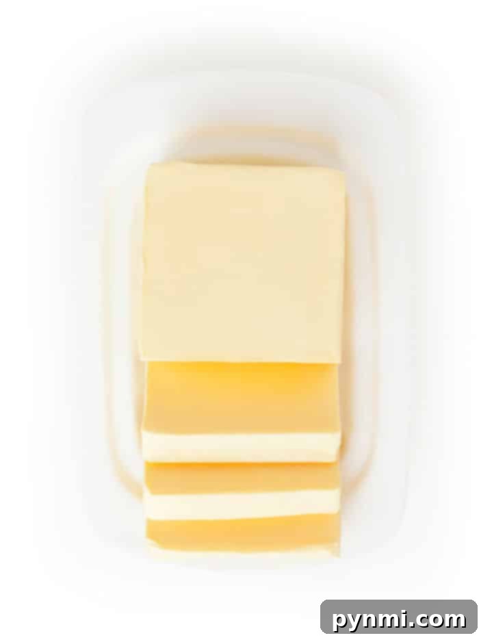 A block of butter with four slices partially cut, showcasing different types of butter, placed on a white dish.