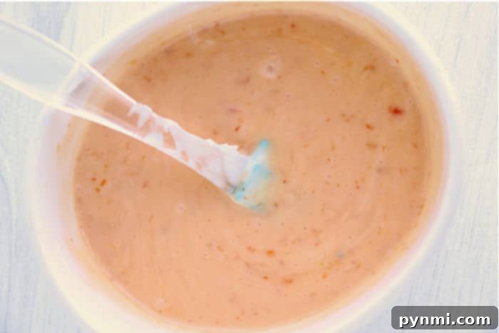 Close-up of a creamy bang bang shrimp sauce with specks, perfect for drizzling over instant pot bang bang shrimp, served in a white bowl with a spoon.