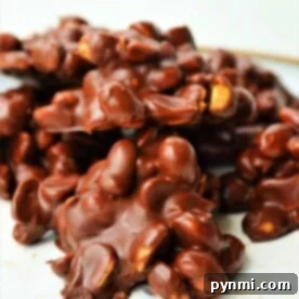 A delightful mound of crockpot chocolate candy sits on a white surface, revealing clusters of nuts beneath the smooth coating.