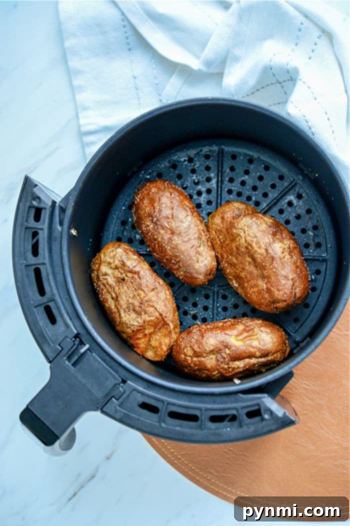 baked potatoes in air fryer - Perfectly baked Russet potatoes resting on a cutting board, ready for the next step in making potato skins.