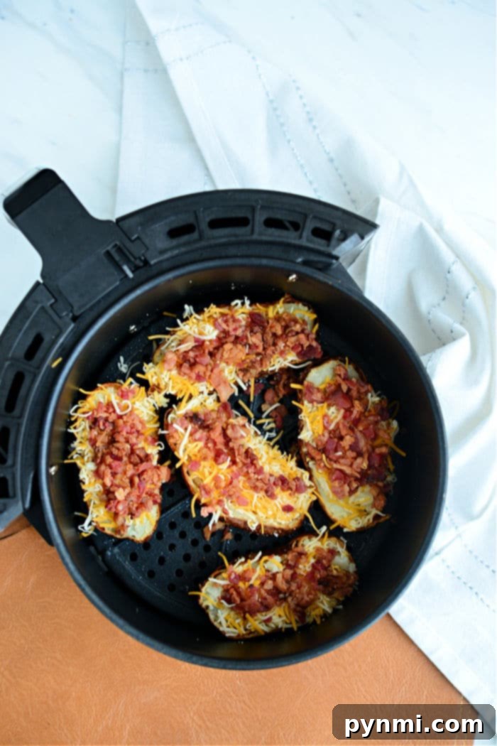 Air fryer potato skins loaded with melted cheese and crispy bacon bits make for the perfect snack. - A white bowl filled with air-fried potato skins, topped with melted cheese, crispy bacon, and a dollop of sour cream, garnished with fresh chives.
