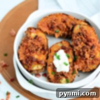 A white bowl contains four air fryer potato skins with crispy cheese and bacon bits, garnished with chopped green onions. One potato skin has a dollop of sour cream.