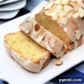 Zesty Lemon Loaf 7 Copycat Starbucks lemon loaf cake with icing and almond slices on a white platter, placed on a blue checkered tablecloth.
