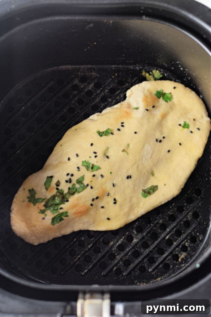 Pillowy Soft Air Fryer Naan 6 Two pieces of air fryer naan bread cooking in an air fryer basket, with nigella seeds and cilantro.