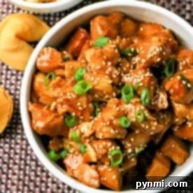 A bowl of flavorful Instant Pot Asian chicken topped with green onions, with fortune cookies and rice in the background.