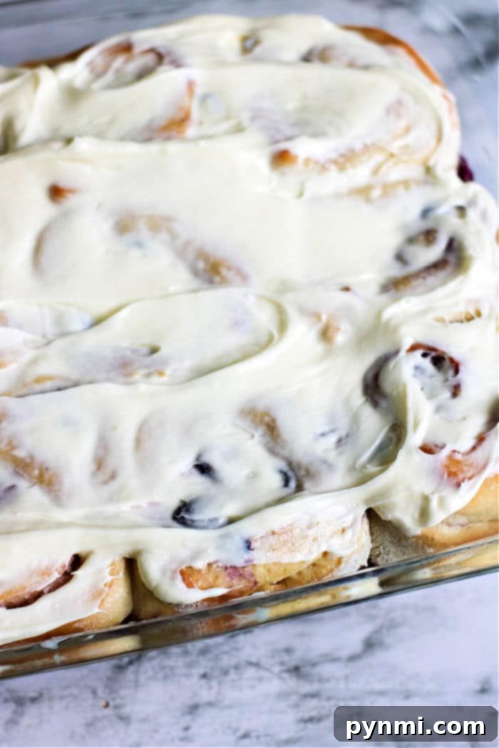 Delicious homemade sweet rolls with a generous layer of white frosting and fresh blueberries on top, arranged in a baking dish.