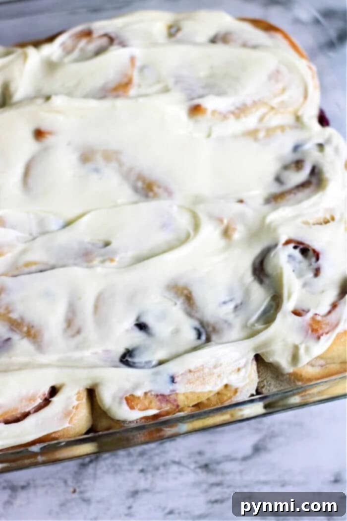 A close-up shot of a single homemade sweet roll with blueberries and frosting on a rustic wooden board.