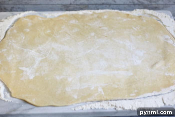 A large rectangular sheet of sweet bread dough, sprinkled with flour, on a wooden surface.