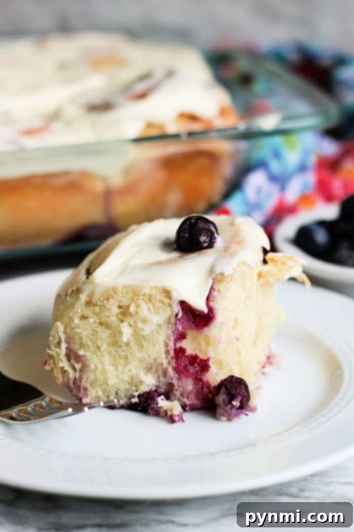 A stack of perfectly baked blueberry sweet rolls, drizzled with white frosting, on a serving plate.