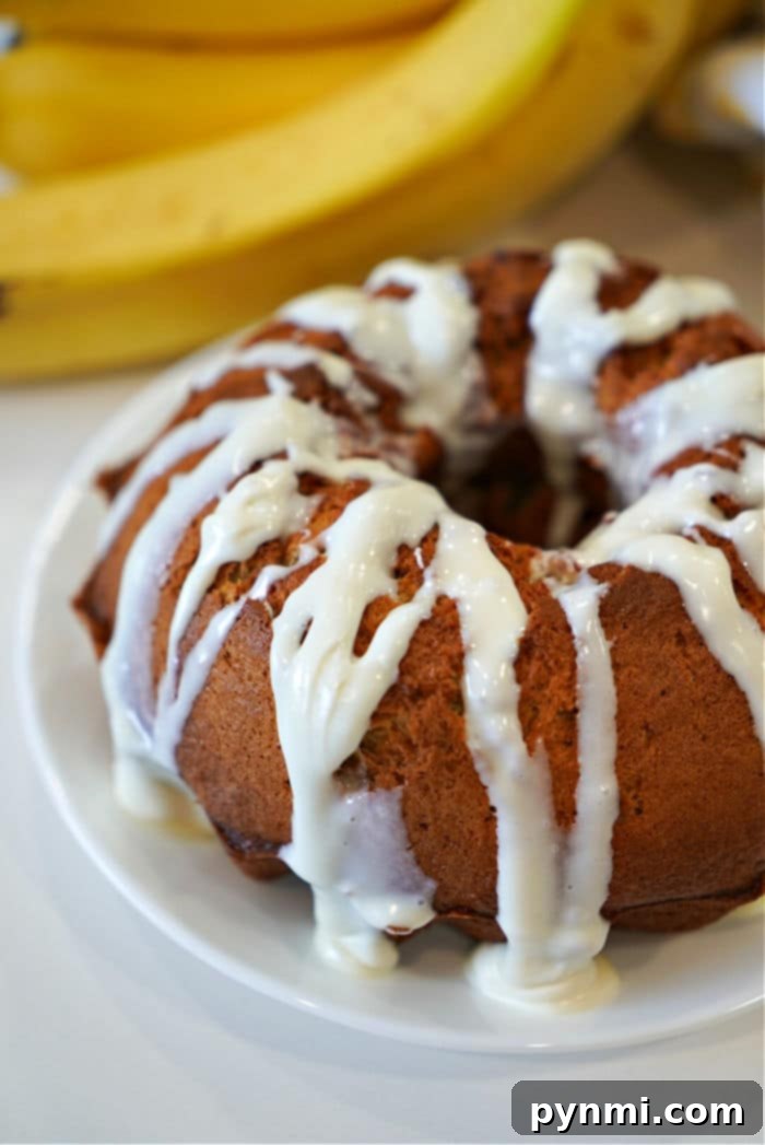 A slice of moist air fryer banana bread on a white plate, with a background of the remaining loaf.