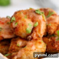 Close-up of crispy, golden-brown air fryer shrimp covered in a savory bang bang sauce, garnished with fresh herbs in a white bowl.