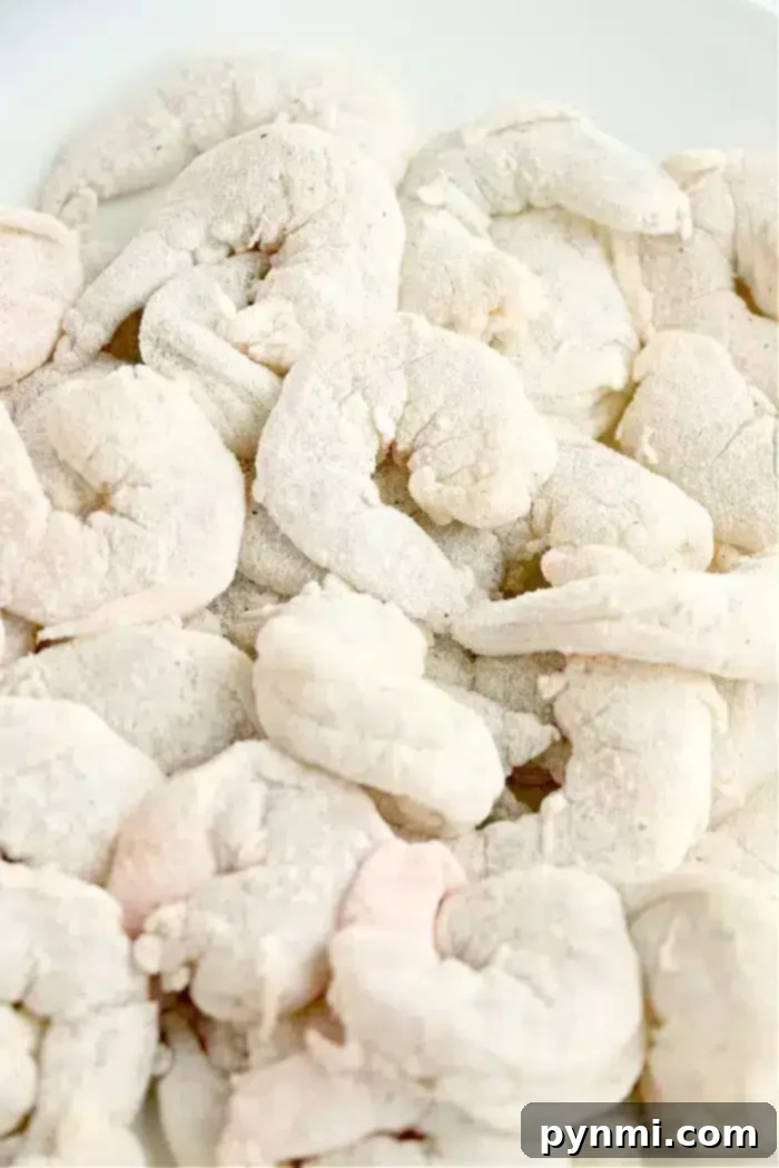 A close-up view of a pile of raw shrimp covered in a layer of flour or breading on a white background, ready to be transformed into crispy air fryer bang bang shrimp.