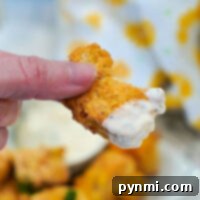 Close-up of a hand holding crispy fried fish with creamy dipping sauce on the edge, reminiscent of perfectly cooked air fryer fish nuggets.