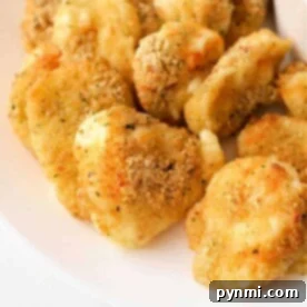 A plate of crispy, golden brown air fryer cheese curds, perfectly seasoned and mouth-wateringly delicious, with a small bowl of marinara sauce partially visible on the side.