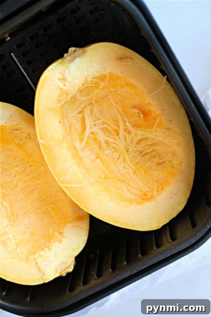 Perfectly Roasted Air Fryer Spaghetti Squash 4 A half of spaghetti squash baking in an air fryer basket, with visible seasonings.