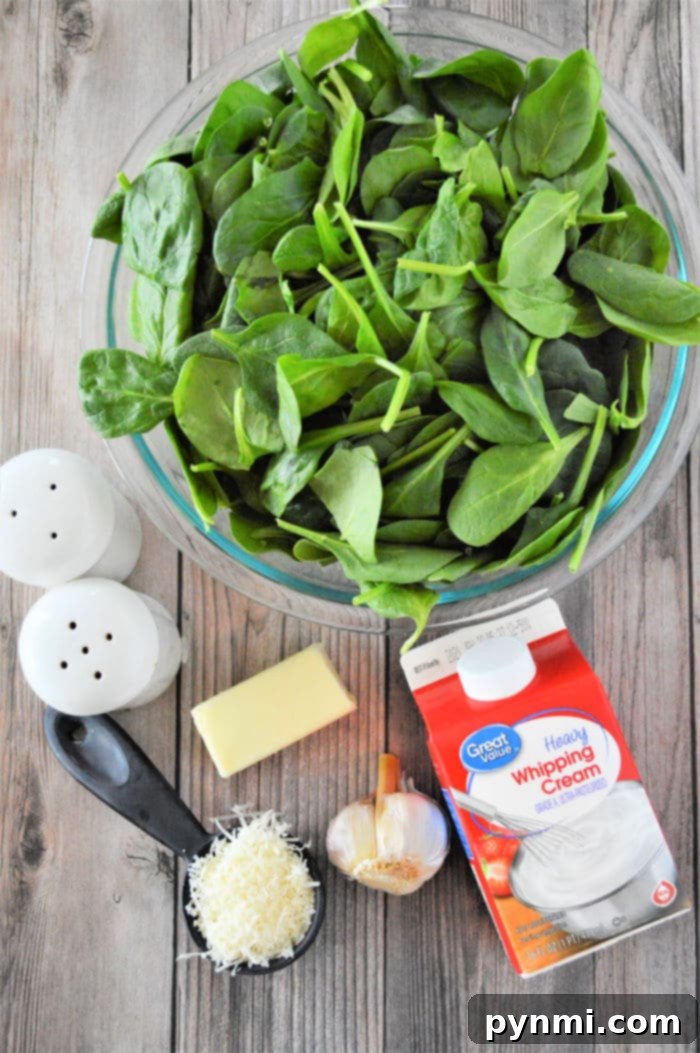 Ingredients laid out for making creamed spinach: fresh spinach leaves, heavy cream, garlic, butter, and Parmesan cheese.