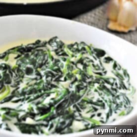 A white bowl filled with creamy spinach, showcasing delicious creamed spinach, with a pan and garlic in the background.