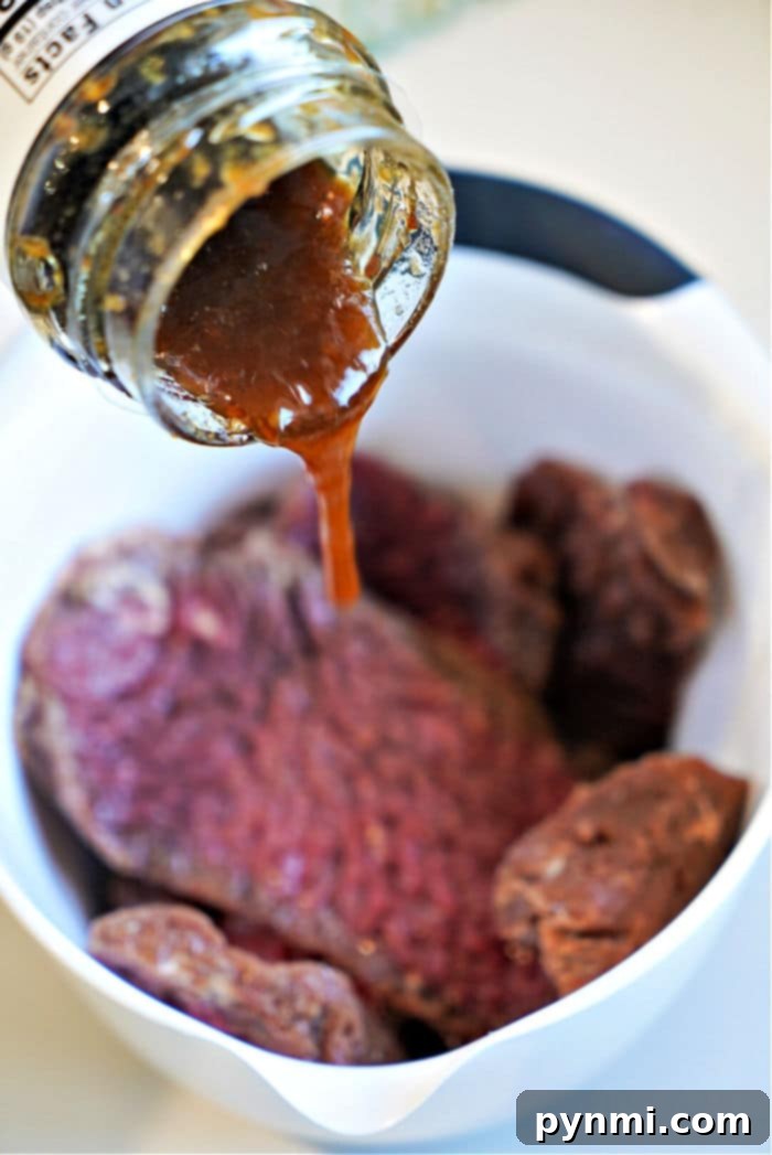 Crispy Golden Air Fryer Cube Steaks 6 Thick teriyaki sauce being generously poured over raw cube steak pieces in a white bowl, beginning the marination process for air frying.