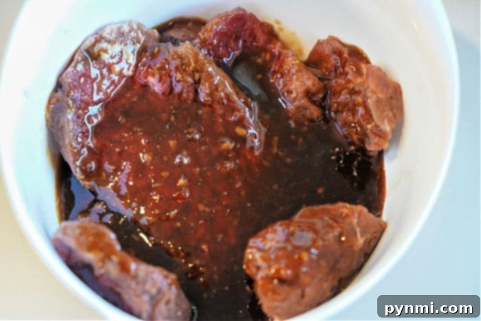 Crispy Golden Air Fryer Cube Steaks 7 Raw cube steak pieces thoroughly marinating in a dark, thick sauce in a white bowl, absorbing flavors for a perfect air fryer meal.