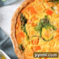 A savory breakfast quiche recipe featuring spinach, red and yellow bell peppers rests on a gray cloth, with colorful peppers nearby.