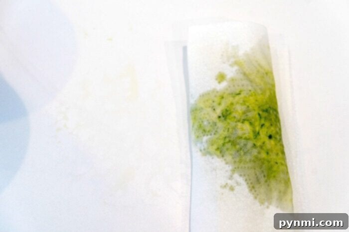 Close-up of a hand grating zucchini over paper towels to remove excess moisture.