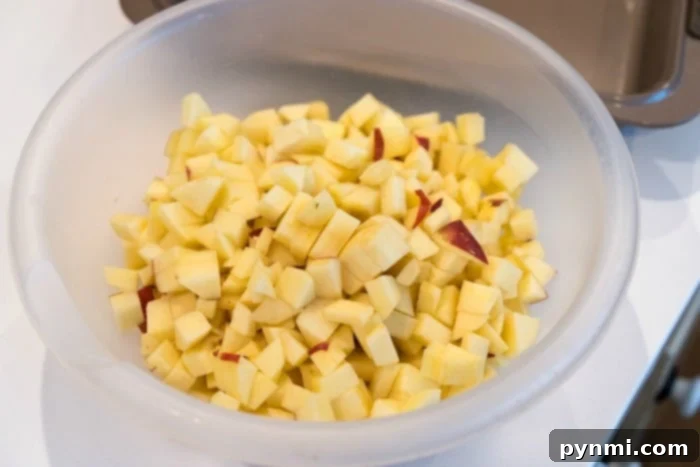 Wholesome Apple Carrot Muffins 3 A bowl filled with diced apples rests on a white countertop, ready for baking.